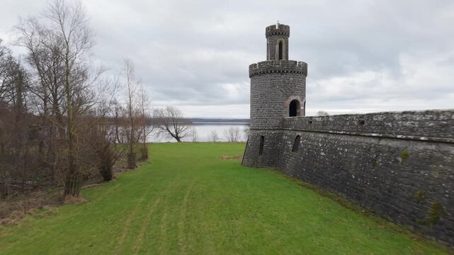 Low aerial flight along the stone wall of Shane's Castle towards a castle turret, with Lough Neagh behind, Northern Ireland