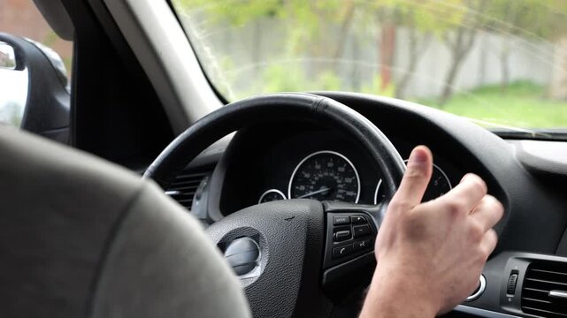 Male arms holds steering wheel while driving a motor car at city. Young man riding on electric automobile at urban road. Driver moving on his electrical auto on route. Slow motion
