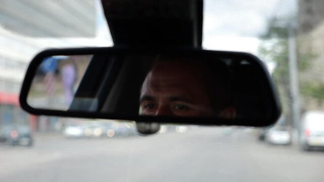 Eyes of male driver reflecting in rearview mirror while riding motor auto. Young man looking concentrated to urban road during operating electric vehicle. Confident guy driving modern car at city