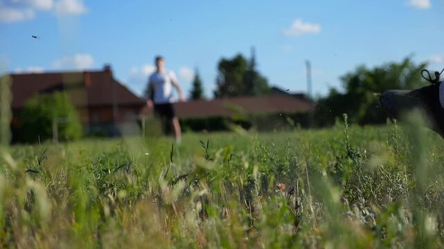 Male foot of footballer kicking a soccer ball while another player tries to catch it background. Leg of sportsman shooting ball on a green field during an intense training session. Freestyle football