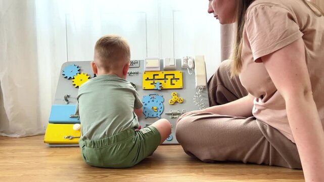 Toddler twisting locks and latches on sensory board. Age appropriate learning toy. Child discovering how everyday objects work. Motor skills training while having fun