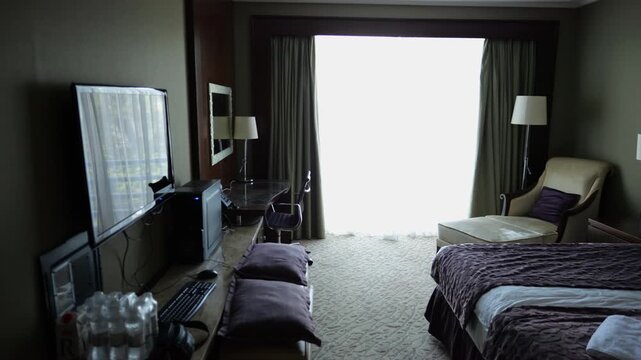 View of modern hotel room interior with neatly arranged bed, soft day lighting and comfortable furniture. Cozy accommodation space designed for relaxation, travel and hospitality service