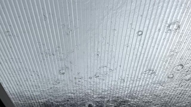Heavy rain pouring on transparent plastic roof canopy. View of large raindrops and flow water stream smashing into corrugated polycarbonate sheet on rainy day. Serene and mood yseasonal weather scene