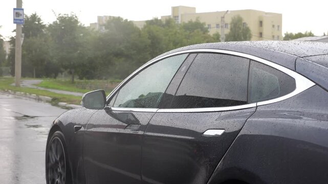 Modern electrical automobile driving at urban road on rainy day. Ecology friendly car riding moving along motorway. Electric vehicle riding through empty highway. Concept of green innovation. Slow mo
