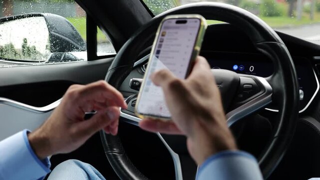 Male entrepreneur browsing modern smartphone while riding autonomous self driving electric car at city. Successful businessman using phone during riding on electrical auto with autopilot at rainy day