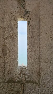 View of the ocean through a narrow medieval loophole window in a stone wall