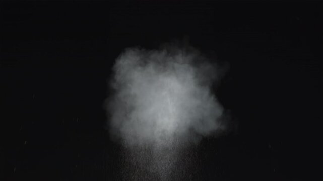 Dusty bullet impact against a wall, sending fragments of debris flying through the air. White powder burst isolated on black background. Explosive hit, scattering dust particles. Cloud of fine debris