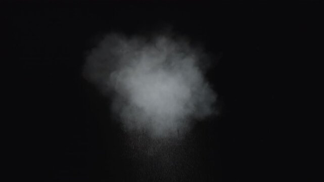 Dusty bullet impact against a wall, sending fragments of debris flying through the air. White powder burst isolated on black background. Explosive hit, scattering dust particles. Cloud of fine debris