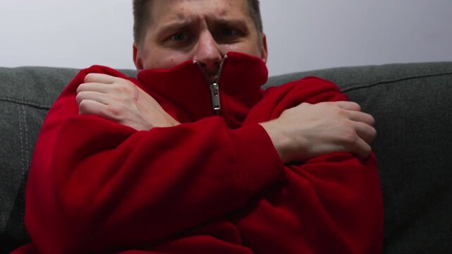 A person is cold.
A man hugs himself with his arms, trying to warm up inside his apartment.
A cold apartment; problems with the heating.