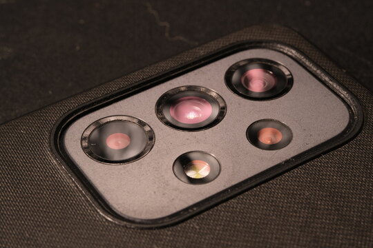 Close up macro shot of a multi-camera array on a modern smartphone, featuring multiple lenses and sensors for mobile photography on a black textured phone case.