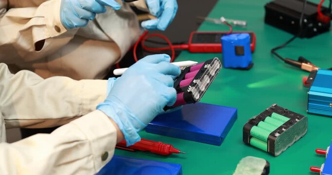 Technician in protective gloves tests a rechargeable battery pack with a probe on an electronics workbench.