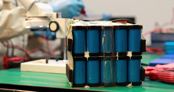 Close-up of a worn blue cylindrical battery pack with exposed wiring on a green workbench in an electronics repair workshop.