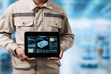 Industrial worker holding a tablet with a digital factory dashboard in a blurred modern production facility. © Phushutter