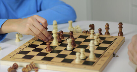 Two players compete in chess match. Hands move wooden pieces across checkered board during focused strategy game indoors. Closeup shows concentration, planning, and competitive thinking. © julia_diak