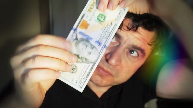 A man checks a hundred dollar bill by feeling it and holding it up to the light.
