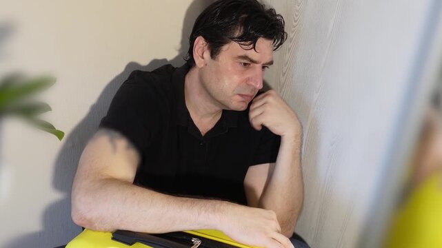 An attractive man leaning on a suitcase tries to fall asleep while waiting for a train.
