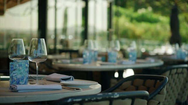 Close-up of a set table with a wine glass, blue patterned tumbler, plates and napkins on an empty restaurant terrace, French Riviera, France.