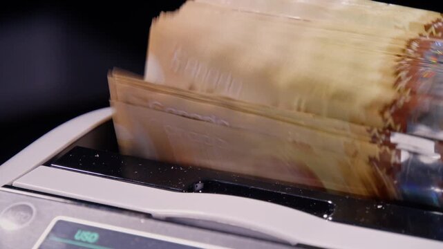 Canadian hundred-dollar bills advance through a counting machine in a swift stream of cash
