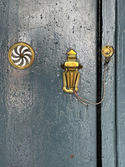 Close-up of antique brass door hardware on a weathered blue wooden door in San Fernando, Cadiz, Spain, showing aged paint and traditional decorative details © MaruStock