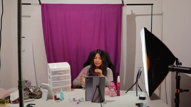Young female content creator filming a makeup tutorial or beauty product review at her home studio, engaging with her online audience and demonstrating cosmetic items