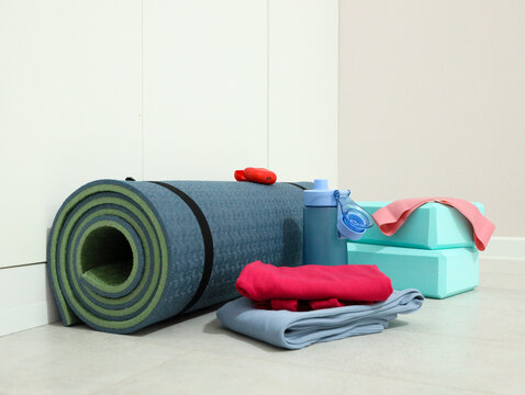 Fitness Accessories Arranged On Clean Floor Beside Plain Wall, Featuring Rolled Mats, Stacked Towels, Water Bottle, Resistance Band And Yoga Blocks, Suggesting Home Workout, Pilates And