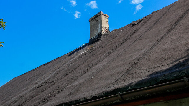 An old brick chimney stands on a dark, weathered roof against a blue sky.