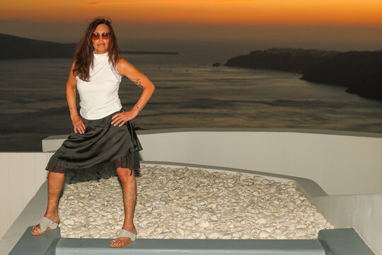 Beautiful middle aged woman at a private swimming pool overlooking the Santorini, Greece caldera during sunset. Luxury travel vacation and lifestyle. 