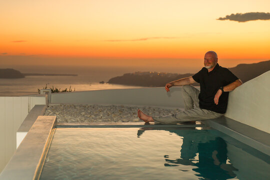 Bald man with a gray beard outside during sunset overlooking the Santorini caldera in Greece. A Greek vacation with an epic view. 