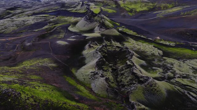 Aerial view showing moss covered volcanic fissures and craters along the Lakagigar row in the highlands of Iceland, revealing rugged volcanic terrain and dirt paths.