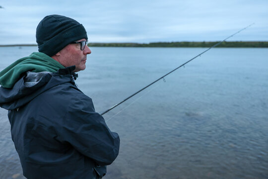 Middle aged man fishing for salmon on the Egegik river in Alaska. The sport fisherman is wearing cold weather clothes and holding a pole in early morning. 