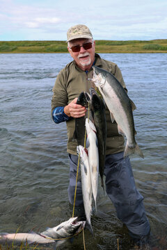 Happy mature man showing off his fresh salmon catch while on vacation. Retirement trip on an Alaskan river with big fish. 