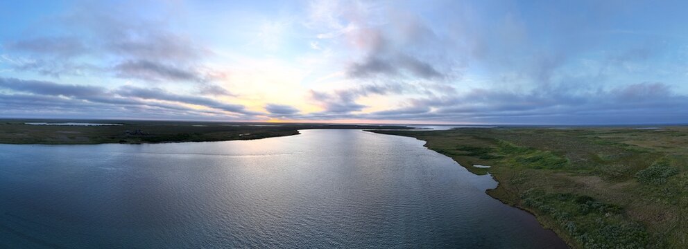 Aerial panoramic view of the Egegik river in Alaska during an evening sunset and a beautiful sky with colorful clouds as the water flows below. 