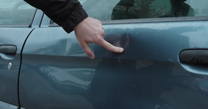 Hand inspecting dents in a car door for vehicle damage and insurance assessment