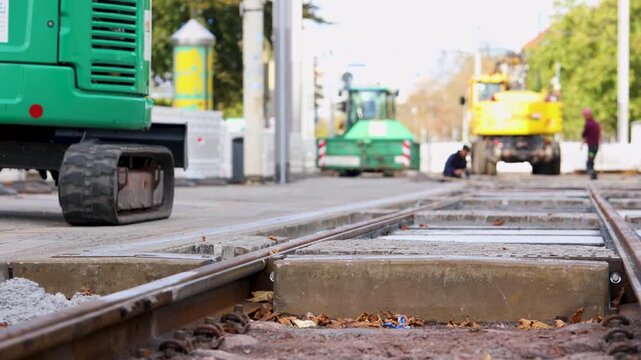 Municipal workers repair tram tracks in Magdeburg, Germany, using excavator and construction machinery. Close view of railway rails and concrete sleepers shows urban infrastructure maintenance