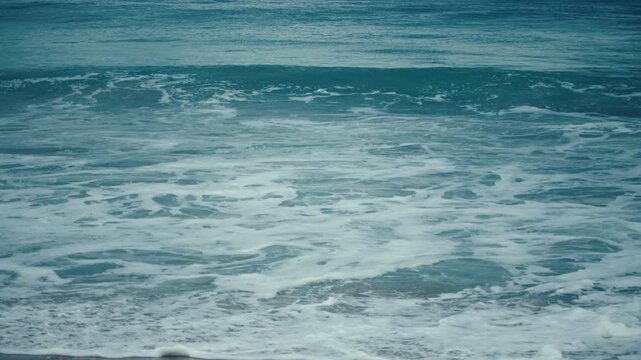 White ocean foam spreads across the surface as powerful Pacific waves roll toward the sandy shore.