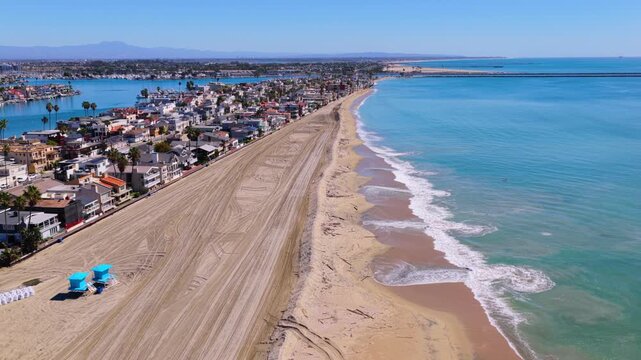 Long Beach, California, USA - October 15, 2026: Camera descends from a wide view to the crest of a new sand berm strewn with storm driftwood, shielding Peninsula homes after Tropical Storm Rachel.