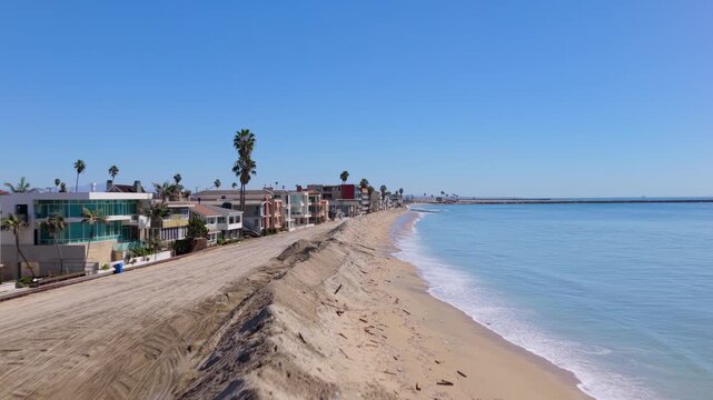 Long Beach, California, USA - October 15, 2026: Low forward flight along the crest of a sand flood berm separating oceanfront mansions from the surf after Tropical Storm Rachel, jetty ahead.