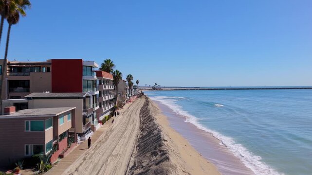 Long Beach, California, USA - October 15, 2026: Low flight along a sand berm past beachfront homes, rising to an excavator extending it toward the broken seawall after Tropical Storm Rachel.