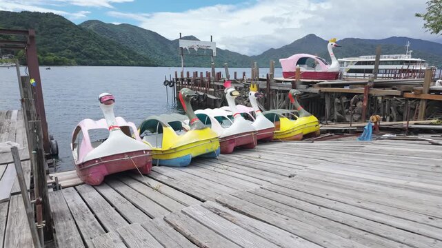 Colorful swan pedal boats docked at a wooden pier on Lake Chuzenji in Nikko, Tochigi, Japan, offering scenic leisure activities for tourists.