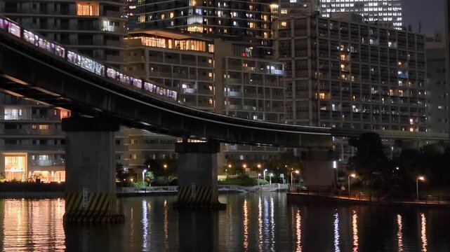 ビルに囲まれた運河の上を通過するモノレールが見える都市の夜景。