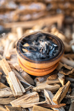 Incense clay pot with burning and smoldering wooden sticks surrounded by Vietnamese cinnamon and agarwood materials in baskets for traditional herbal incense making popular in Vietnam culture.
