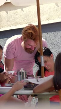 Diverse group of friends sharing outdoor meal under umbrella celebrating togetherness