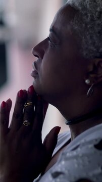 Hopeful African American woman clasping hands in prayer outdoors, feeling optimism