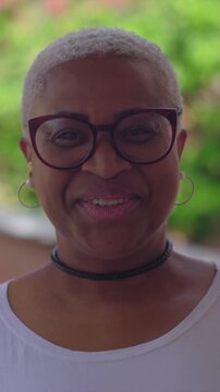 Portrait of confident Afro-Latina woman with glasses smiling warmly outdoors against lush greenery