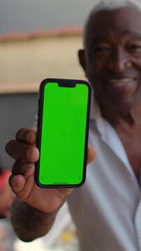 Confident African American elderly man holding green screen smartphone outdoors, app display