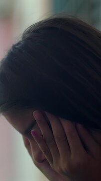 Distressed young girl with brown hair covering face against wall outdoors, feeling sorrow