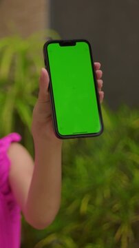 Hand holding vertical smartphone green screen outdoors, mobile app mockup