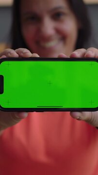 Happy woman presenting green screen smartphone to camera outdoors, mobile app mockup