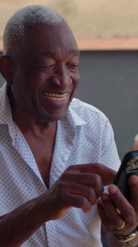 Joyful African American elderly man smiling while using smartphone at outdoor gathering