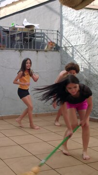 Playful kids jumping over spinning broom in backyard patio, carefree family fun